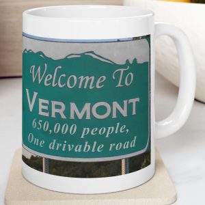 White Mug with fake state motto for Vermont: "650,000 people, One drivable road."